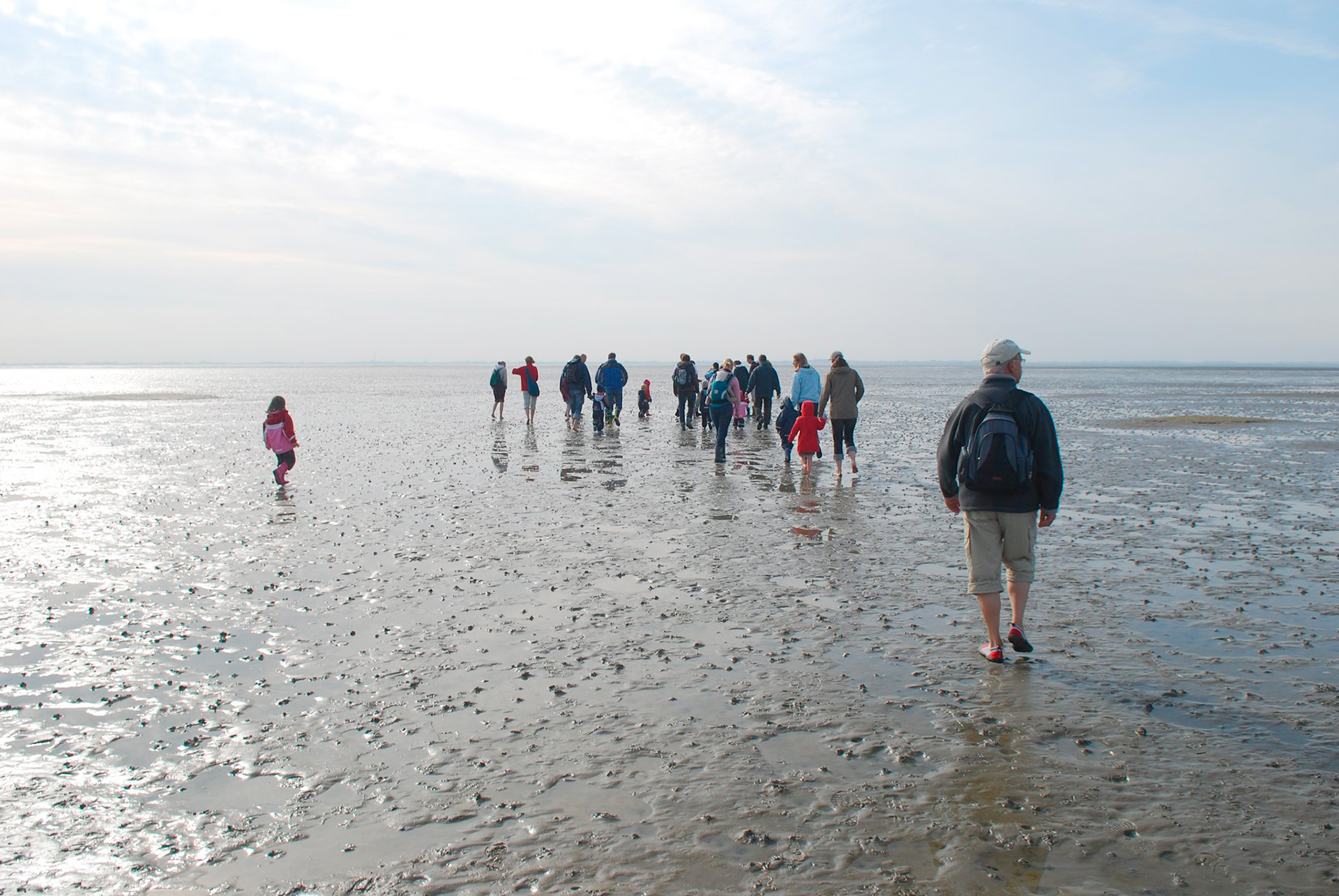 Eine Gruppe von Menschen wandert durch das Watt. Ihre Hosen sind hochgekrempelt.